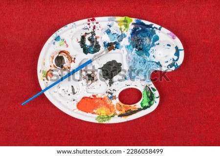 Creative Painter's Palette with Dried Paint and Brush on Red Background