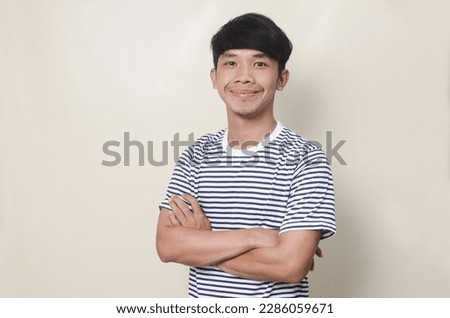Young confident smiling asian man standing with crossed arms gesture over isolated background