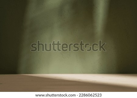 Empty table on khaki green texture wall background. Composition with monstera leaves shadow on the wall and light reflections. Mock up for presentation, branding products, cosmetics food or jewelry.