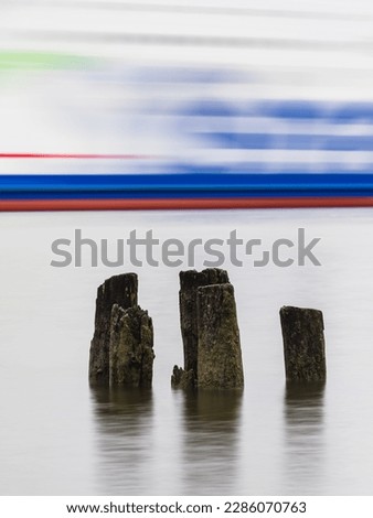 A long exposure photo of a ferry drifting behind wooden poles in the peaceful Göta River in Gothenburg, Sweden.