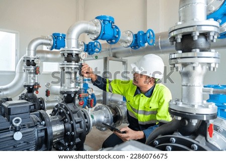 A worker at a water supply station inspects water pump valves equipment in a substation for the distribution of clean water at a large industrial estate. Water pipes. Industrial plumbing. Royalty-Free Stock Photo #2286076675