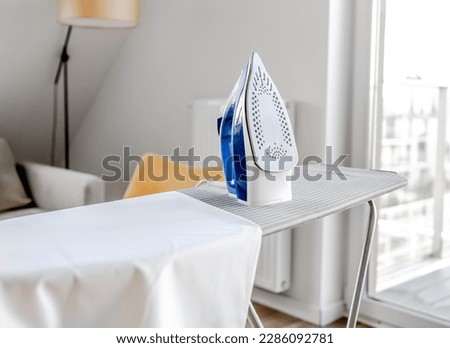 Electrical iron for wrinkled clothes on ironing board indoor. Modern home appliance tool for housekeeping Royalty-Free Stock Photo #2286092781