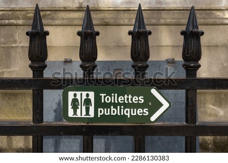 Green public toilet sign in French on a fence in Paris, France.