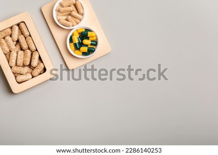 Vitamins and nutrients supplements in small wooden box and minerals capsules on wooden desk from above on light background. Minimalistic picture with vitamins to protect health from illnesses.