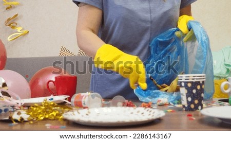 woman cleaning the house after a birthday party chaos, messy in livving room at home, table with pizza and glasses covered with confetti, ballons, chair on the floor at morning after party celebration Royalty-Free Stock Photo #2286143167
