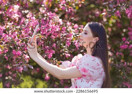  girl , makes selfie on smartphone, is standing in a blooming garden