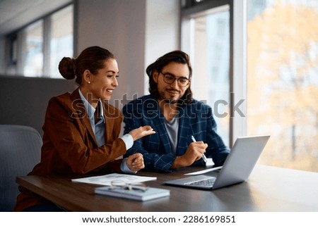 Young happy entrepreneurs cooperating while working on laptop in the office. Royalty-Free Stock Photo #2286169851