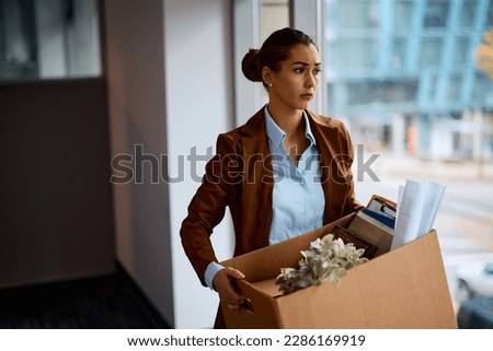 Sad businesswoman with box of her belongings leaving the office after being fired from her job. Royalty-Free Stock Photo #2286169919