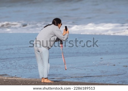 Teenage girl taking pictures of the sea with her cell phone at the beach