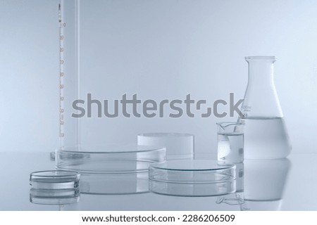 Minimal background with laboratory glassware containing colorless liquid decorated on white background. Two petri dishes upside down form empty platforms to cosmetic product presentation. Front view. Royalty-Free Stock Photo #2286206509