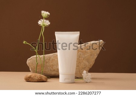 Minimal concept with stones and flower and white plastic bottle without label on brown background. Mockup for cosmetic product, facial moisturizer cream or facial cleanser. Front view Royalty-Free Stock Photo #2286207277