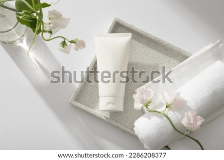 Unlabeled white tube displayed on a square tray with rolled towel, a glass transparent flower vase. White cosmetic tube for face cream, cleanser, body lotion or shampoo Royalty-Free Stock Photo #2286208377