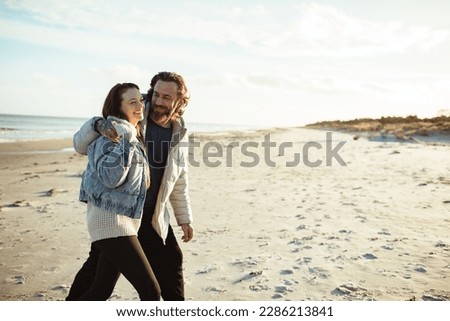 Young adult couple walking on a beach during cold weather Royalty-Free Stock Photo #2286213841