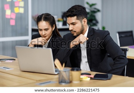 Millennial Asian Indian professional bearded male businessman female businesswoman employee staff in formal business suit sitting working typing laptop notebook computer in company office workplace.