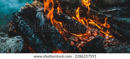 Vivid smoldered firewoods burned in fire close-up. Atmospheric warm background with orange flame of campfire and blue smoke. Full frame image of bonfire. Beautiful whirlwind of embers and ashes in air Royalty-Free Stock Photo #2286237591