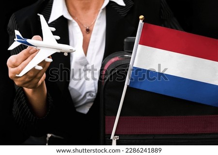 business woman holds toy plane travel bag and flag of Netherlands 