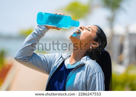 Thirsty woman drinking water from bottle after workout at park - concept of hot determination, heat wave and active lifestyle