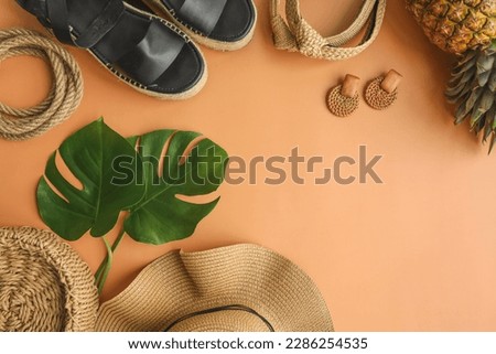 Colorful summer female fashion outfit flat-lay. Straw hat, bamboo bag, wicker shoes, pineapple over beige background, top view, wide composition. Summer fashion, holiday concept.