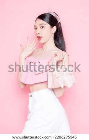 Cute Asian woman model gathered in ponytail with korean makeup style on face have plump lips and clean fresh skin wearing pink camisole holding handbag on isolated pink background. Royalty-Free Stock Photo #2286295345