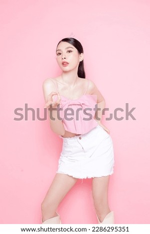 Cute Asian woman model gathered in ponytail with korean makeup style on face have plump lips and clean fresh skin wearing pink camisole on isolated pink background.