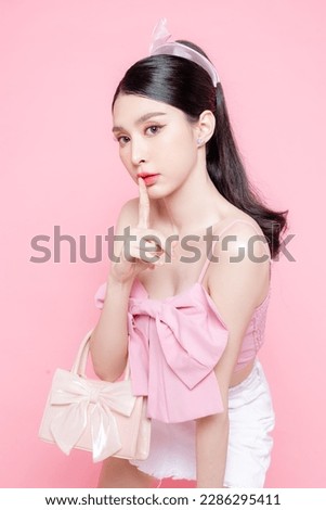 Cute Asian woman model gathered in ponytail with korean makeup style on face have plump lips and clean fresh skin wearing pink camisole holding handbag on isolated pink background.