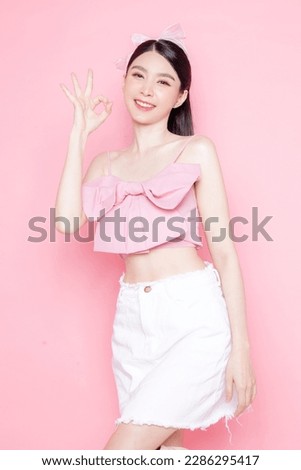 Cute Asian woman model gathered in ponytail with korean makeup style on face have plump lips and clean fresh skin wearing pink camisole show OK sign on isolated pink background. Royalty-Free Stock Photo #2286295417