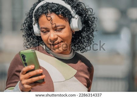latin girl with afro hair with headphones and mobile phone in the street