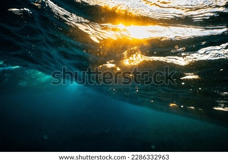 Underwater photo from beneath a wave sparkling from the sunset. Aqua water mixed with golden sunset.