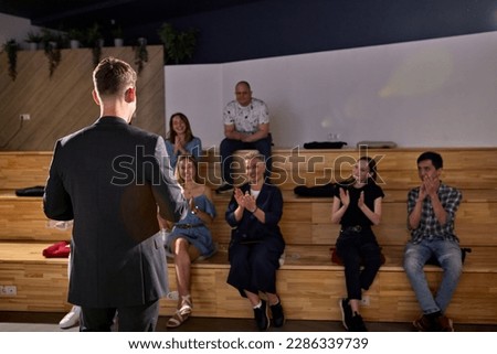 happy group of people clapping hands after listening the conference in lecture hall. Rear view on successful caucasian male speaker in formal black suit. focus on male, view from back. copy space