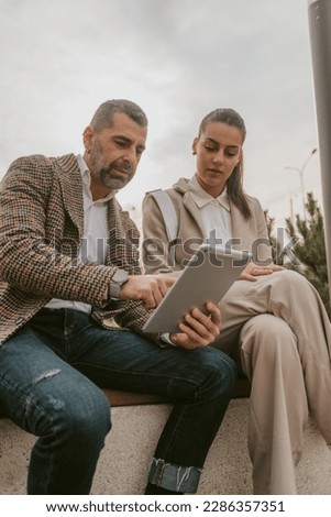 Business colleagues working while sitting at the bench outside