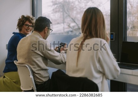 Three inter-generational colleagues working together at the office and having fun conversation. Middle-aged businesswoman smiling