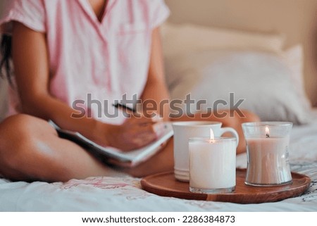 Notebook, writing and woman with home candles for healing journal, calm planning or self care inspiration in bedroom. Creative person or writer for mindfulness goals, meditation or peace notes in bed Royalty-Free Stock Photo #2286384873