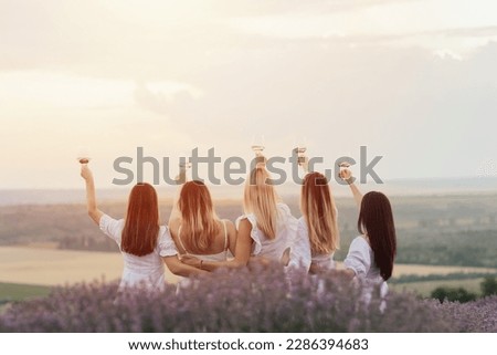 Beautiful girlfriends having picnic in the lavender field in summer sunset. They standing with hands up and enjoying beautiful landscape.	
