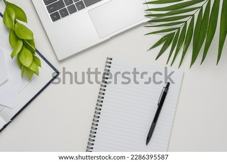 Workspace with blank notebook, laptop, office supplies and green leaves on white background.