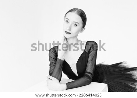 a portrait of a ballerina in a black tutu standing at a cube in a photo studio