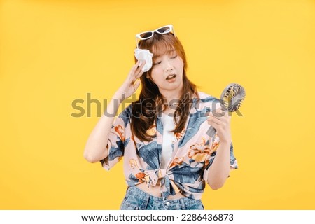 A woman feel hot holds paper tissue and using a portable fan on yellow background