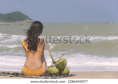 Beautiful woman in swimsuit bikini sitting at the beach by the sea. Wind blow from the sea feel good.
