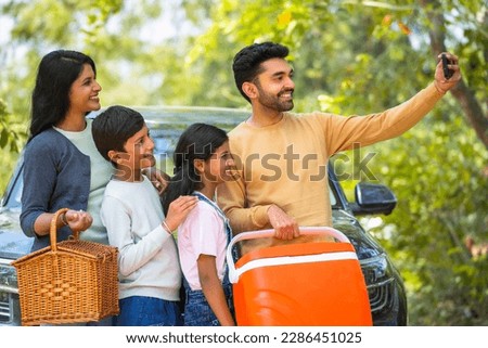 Happy smiling couple with kids taking selfie on mobile phone during summer camp picnic in front of car - concept of family trip, weekend holidays and togetherness. Royalty-Free Stock Photo #2286451025