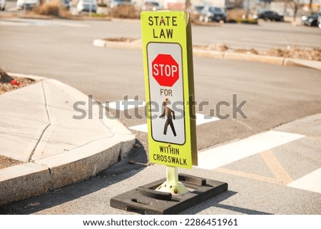 A yellow pedestrian walking sign typically symbolizes that it is safe for pedestrians to cross the street. It is a universal sign of caution and safety for pedestrians. Royalty-Free Stock Photo #2286451961