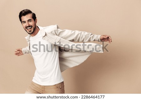 Stylish man smile runs and jumps on a beige background in a white t-shirt and business jacket, flying clothes hero, fashionable clothing style, copy space, space for text Royalty-Free Stock Photo #2286464177