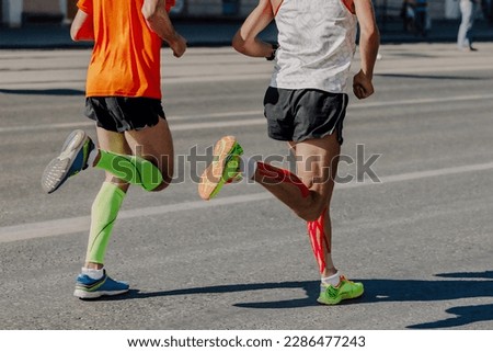 back two athletes runners running marathon in city, legs man jogger in compression sleeves and kinesiotaping calf muscle