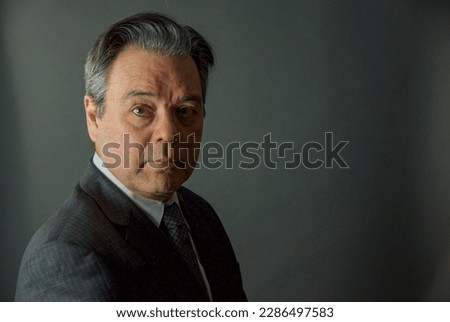 A man in a business suit looks seriously at the camera with a gray background Royalty-Free Stock Photo #2286497583