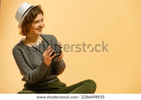 Attractive stylish young girl takes photos with a retro camera isolated on a beige background