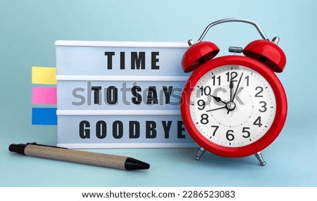 Text TIME TO SAY GOODBYE? written on the lightbox with alarm clock and colorfull stickers on blue background