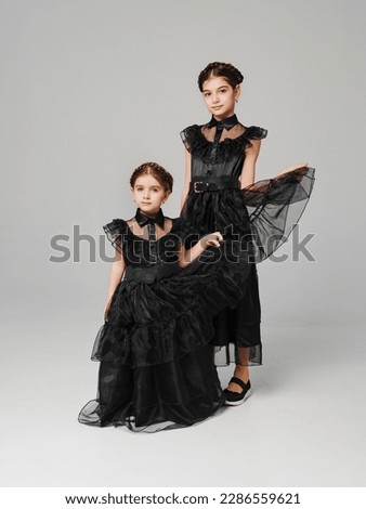 two cute girls in a black long curvy dress on a gray background. the concept of elegant clothes for children. cosplay.