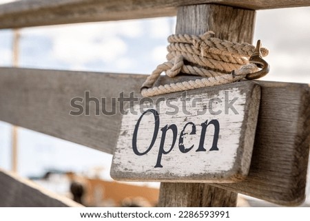 Painted open sign tied with rope to wooden fence