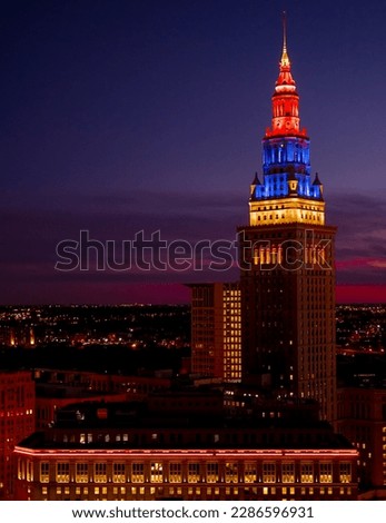 Night view of Cleveland cityscape covered in blue, purple and red shades at night with late sunset and illuminated buildings and suburbs in the background