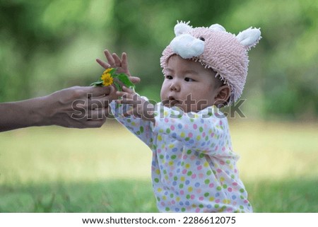 Happy 9 months old baby girl with yellow flowers given by mom, good rest time at the summer garden, Mother's Day Royalty-Free Stock Photo #2286612075