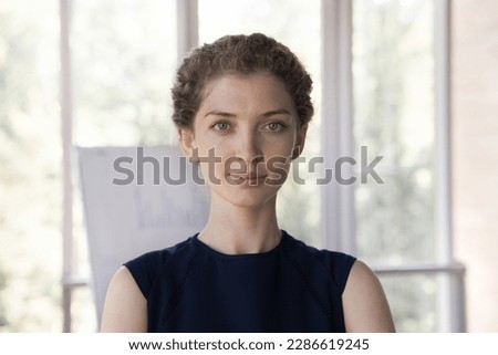 Beautiful curly haired young business woman head shot face portrait. Serious positive successful office professional, confident employee, manager posing for profile picture, looking at camera