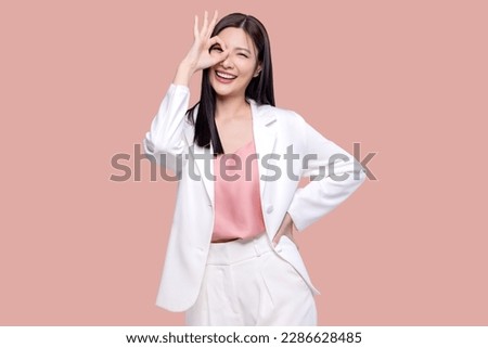 Portrait happy Asian woman shows ok hand sign and looking at the camera on pink background.